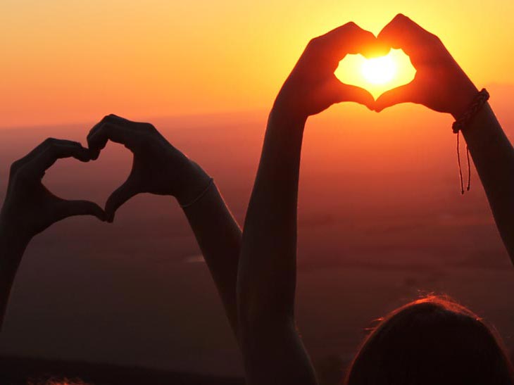 Zwei Schüler bilden mit ihren Händen zwei Herzen vor einem Sonnenuntergang