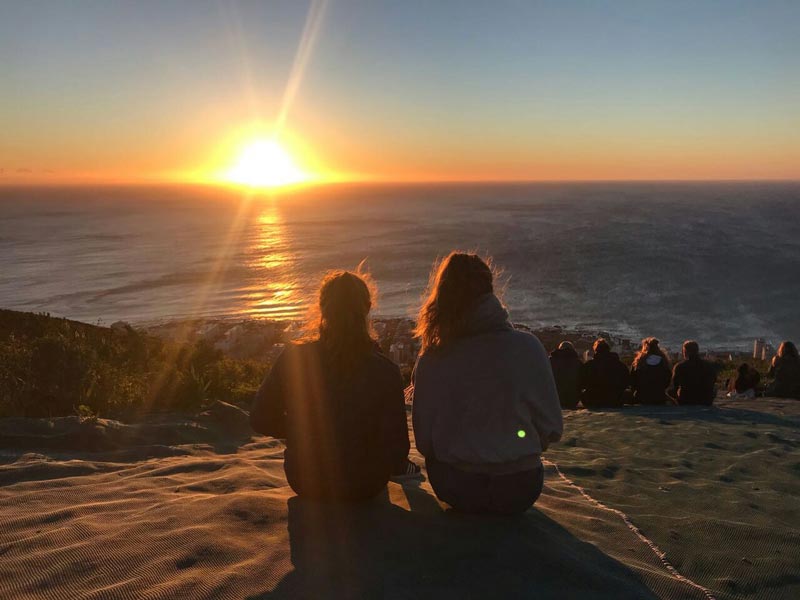 Zwei Freundinnen sitzen im Sand am Strand und schauen sich den Sonnenuntergang an